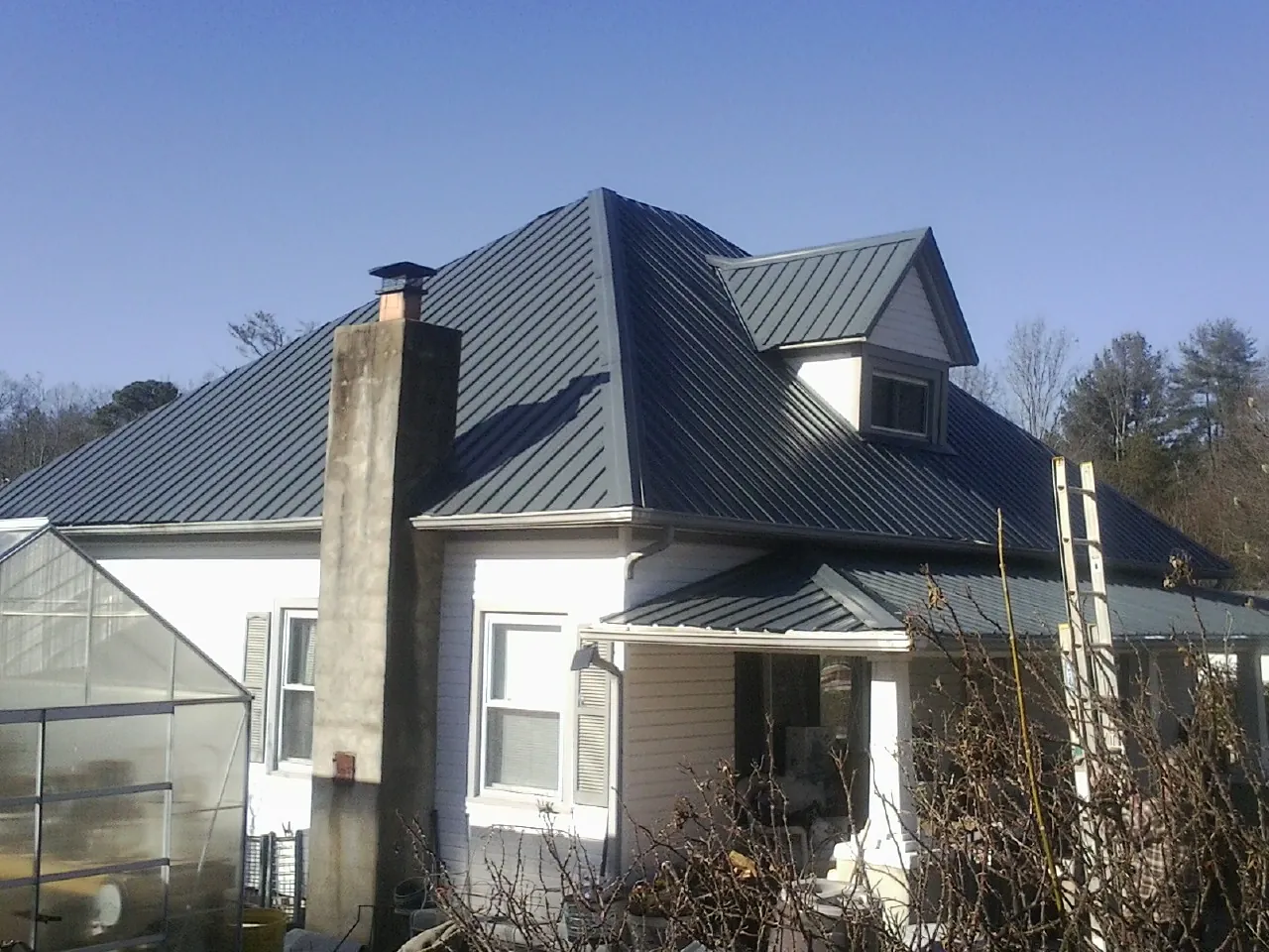 Dark blue standing seam metal roof on a white farmhouse with dormer — Slate & Tile Roof Repair by Roofing Brothers in Waldron
