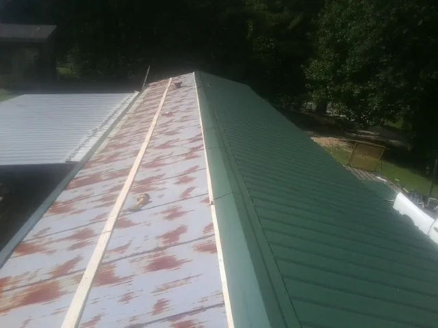 Old rusted panels beside newly installed green metal roofing — Wind Damage Roof Repair by Roofing Brothers in Waldron