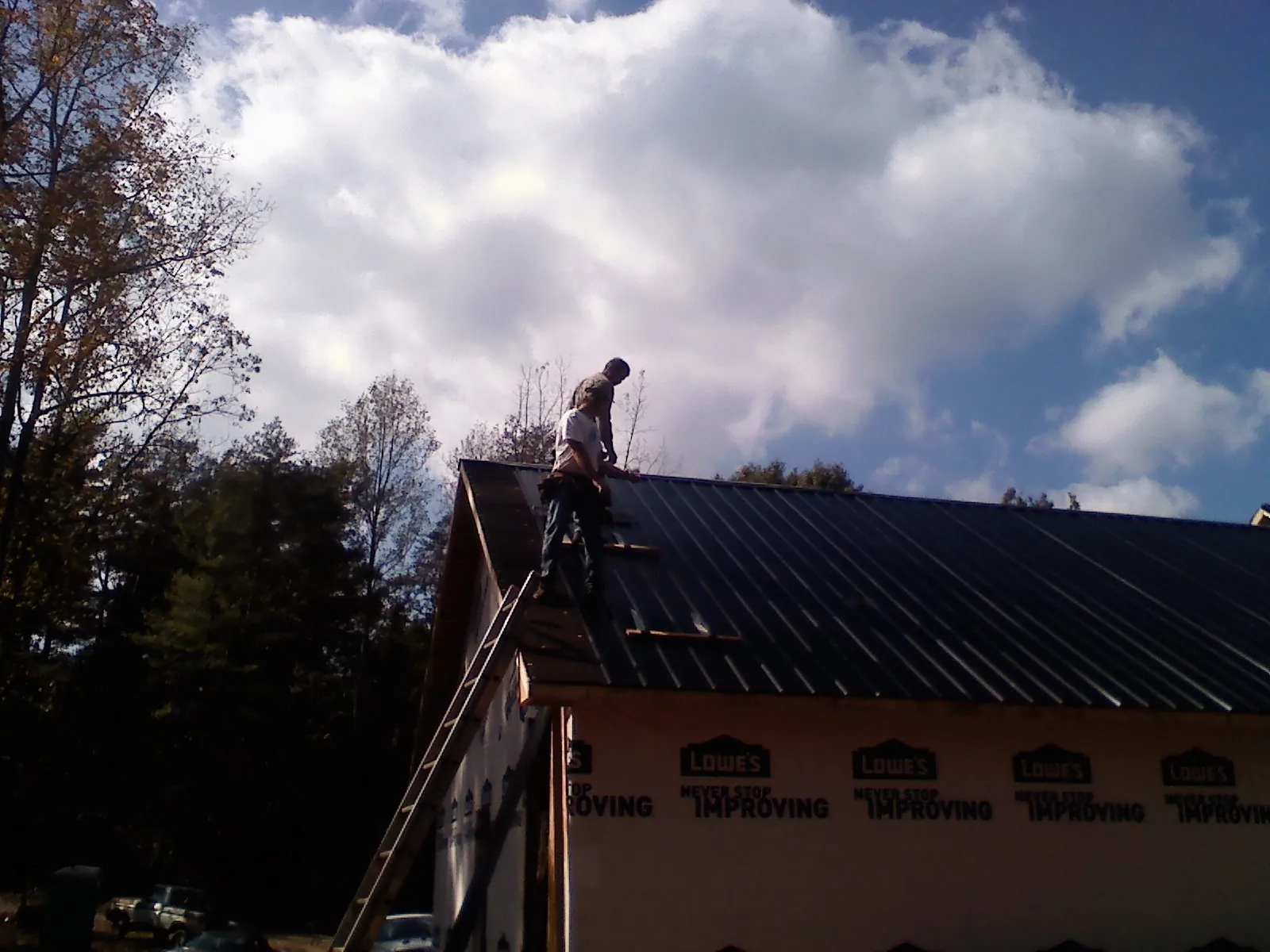 Roofer fastening dark metal panels high against a cloudy sky, from a Roof Inspection job in Waldron